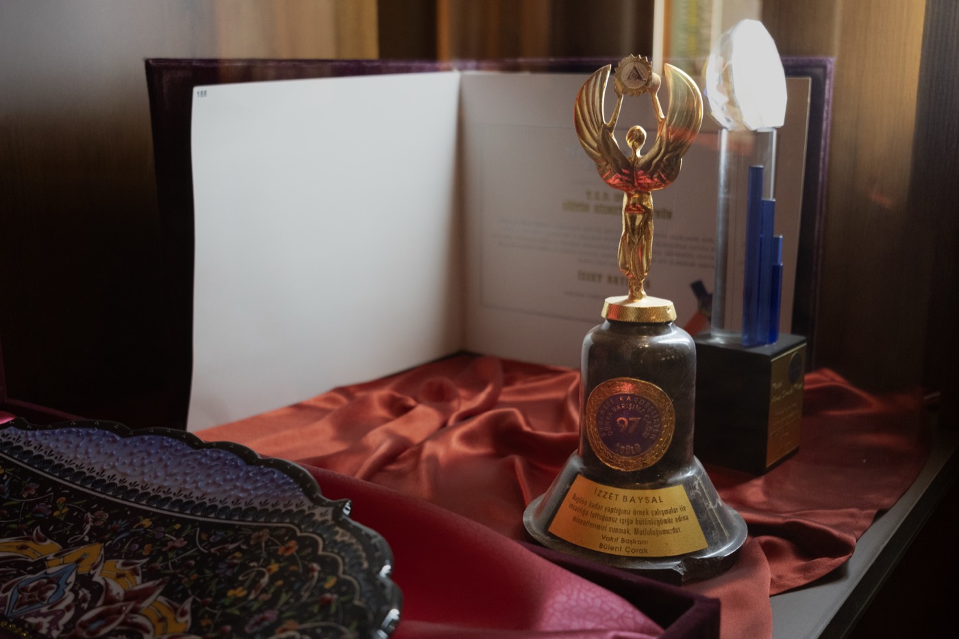 Alt raftaki çan biçimli ödül, yanında çini tabak ve kristal plaket