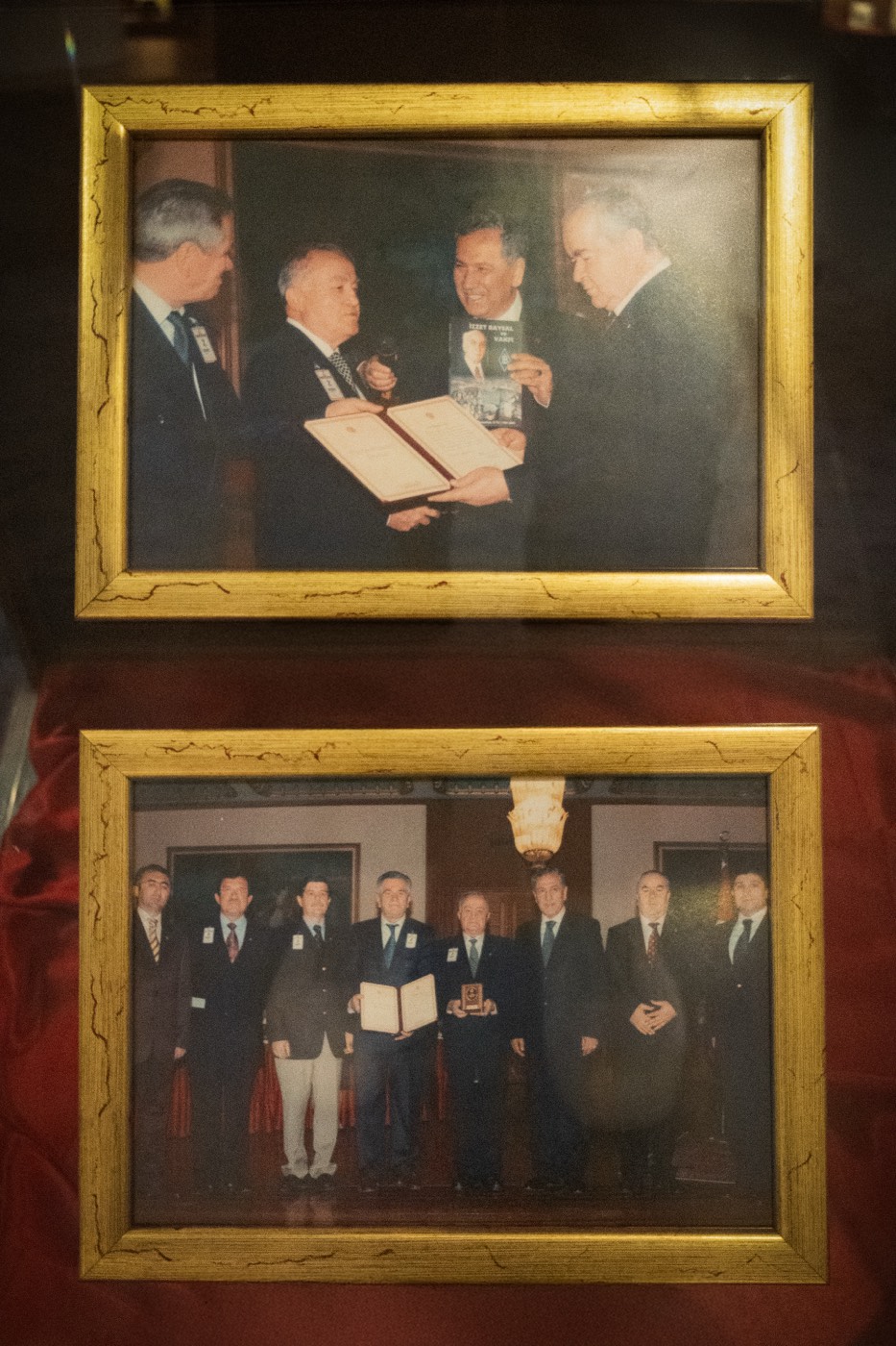Kırmızı saten üzerinde üst üste duran iki çerçeveli tören fotoğrafı
